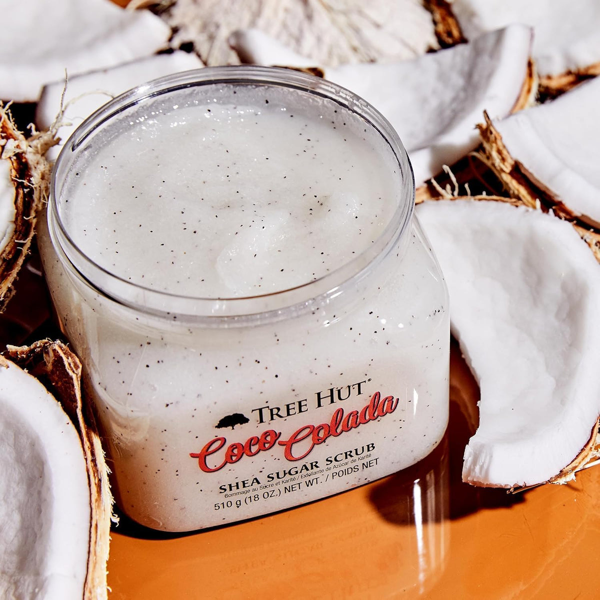 a picture of Tree Hut Coco Colada Shea Sugar Scrub 18oz without lid surrounded by sliced coconut on a solid orange floor