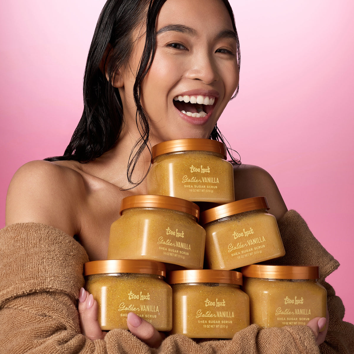 asian woman holding 6 tubs of Tree Hut Golden Vanilla Shea Sugar Scrub 18oz in a triangular shape 