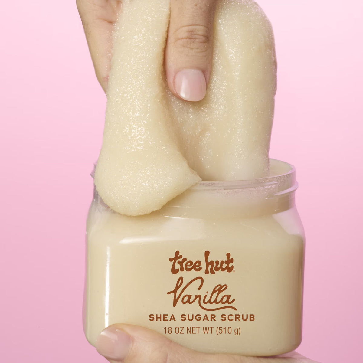 picture of hand picking up Tree Hut Vanilla Shea Sugar Scrub 18oz, showcasing consistency when apply product on a light to solid pink background