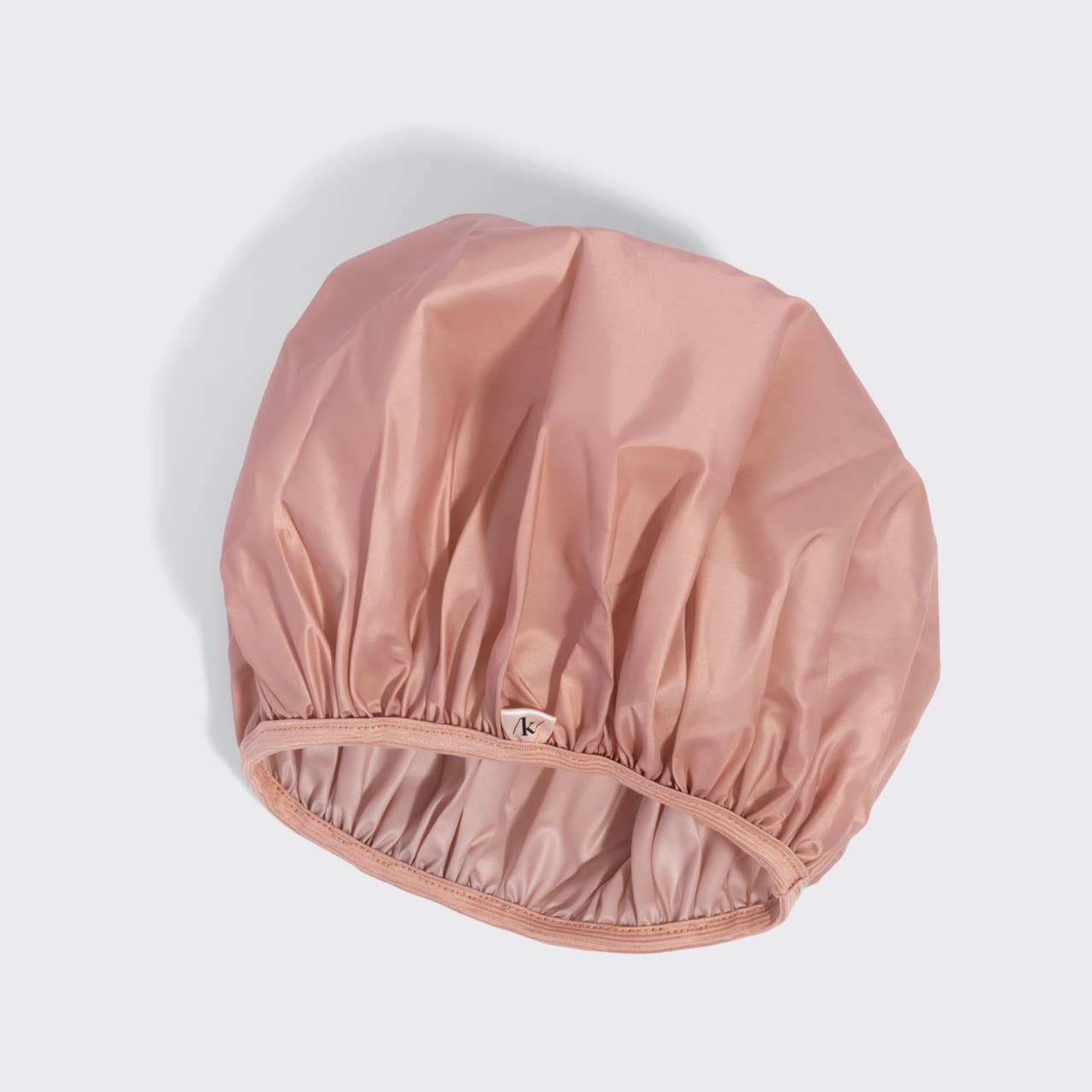 A dusty pink satin shower cap with an elasticized gathered edge, shown on a light gray background with a soft shadow.