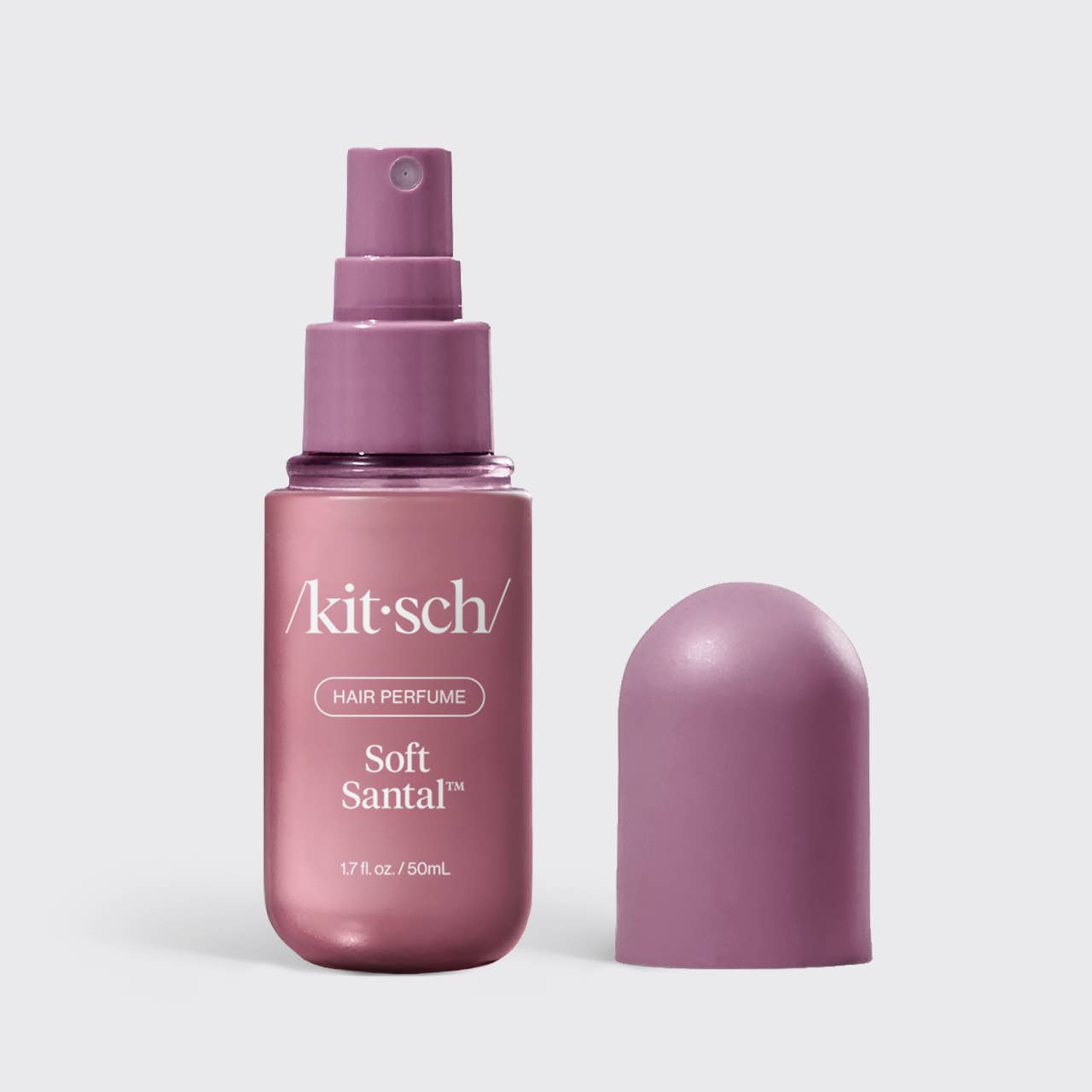 Kit Sch Soft Santal hair perfume in a metallic mauve spray bottle with its cap placed beside it on a light gray background.