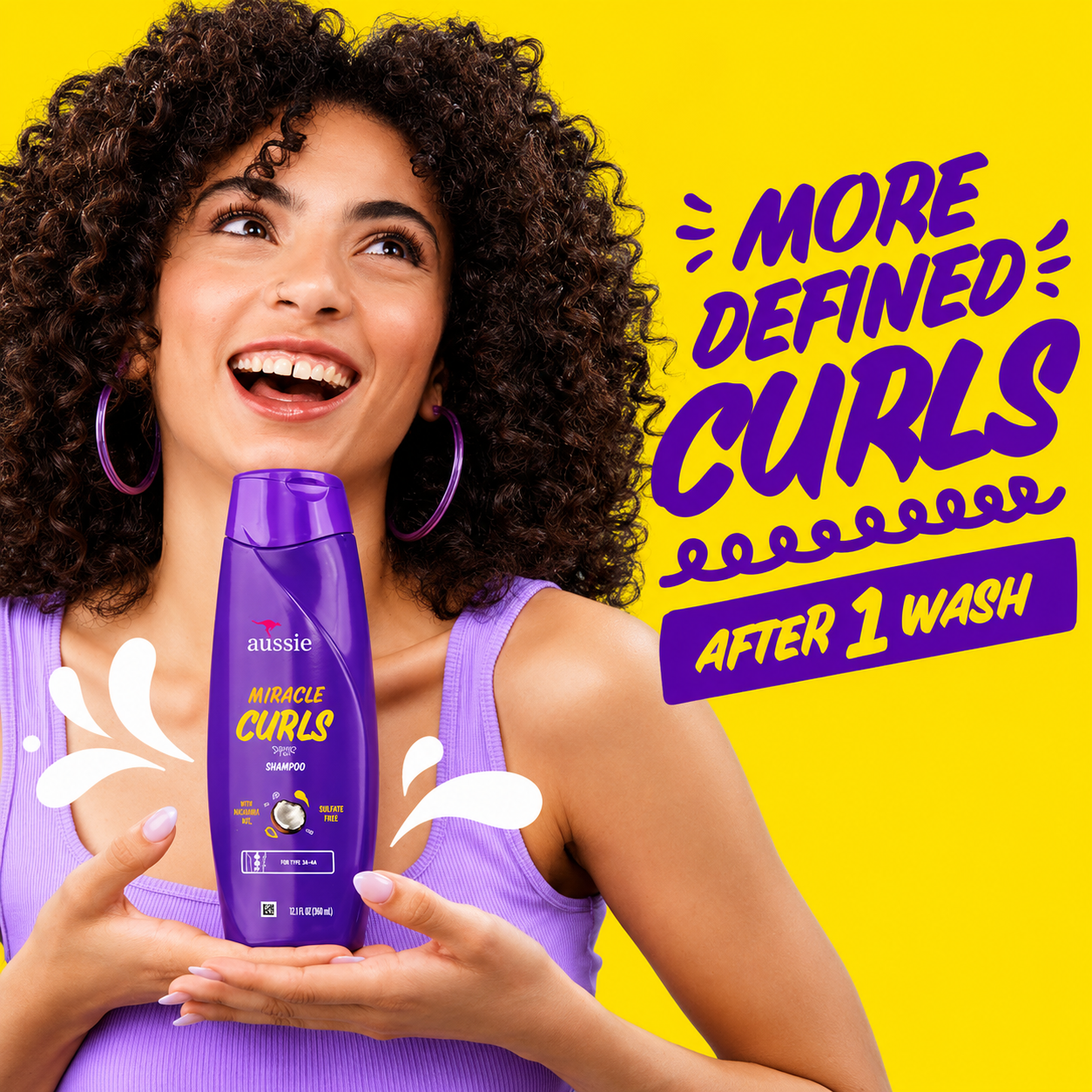 a promotional image featuring a smiling woman with defined curly hair holding aussie miracle curls shampoo in a purple bottle against a bright yellow background. bold text reads "more defined curls after 1 wash", highlighting curl definition and gentle cleansing with playful splash graphics.