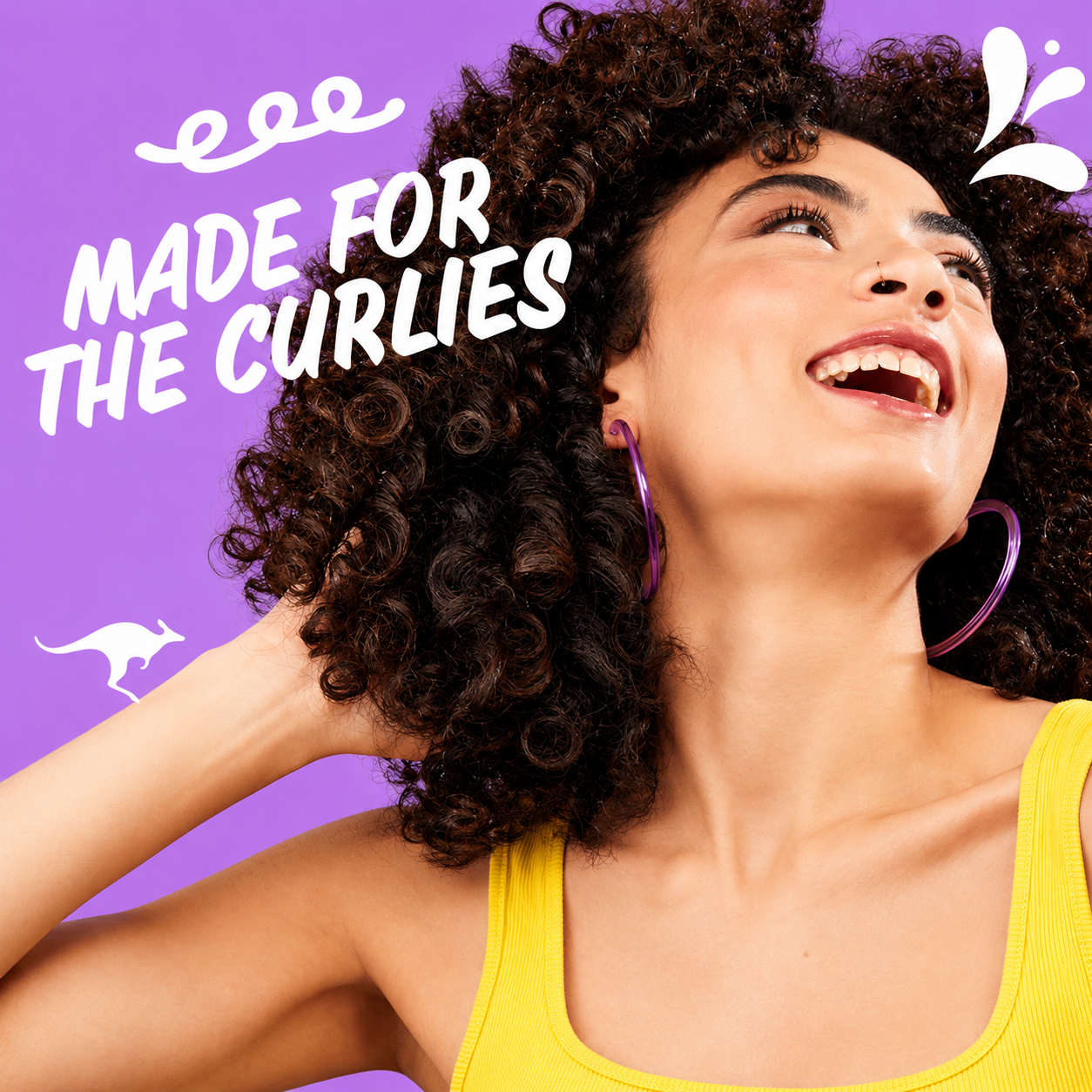 a promotional image featuring a smiling woman with naturally curly hair against a purple background. bold white text reads "made for the curlies" with playful graphic elements, celebrating naturally defined curls and curl-friendly hair care.