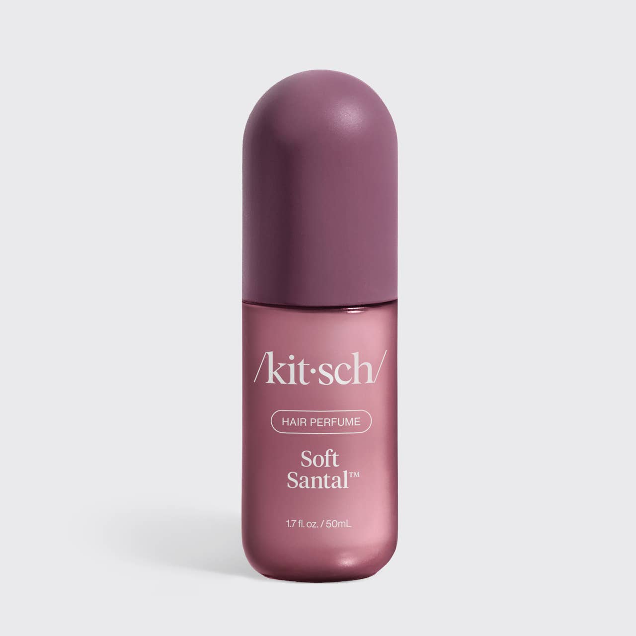 A bottle of kitsch Soft Santal hair perfume, featuring a dusty purple cap and a metallic mauve-pink bottle with white text, set against a light gray background.