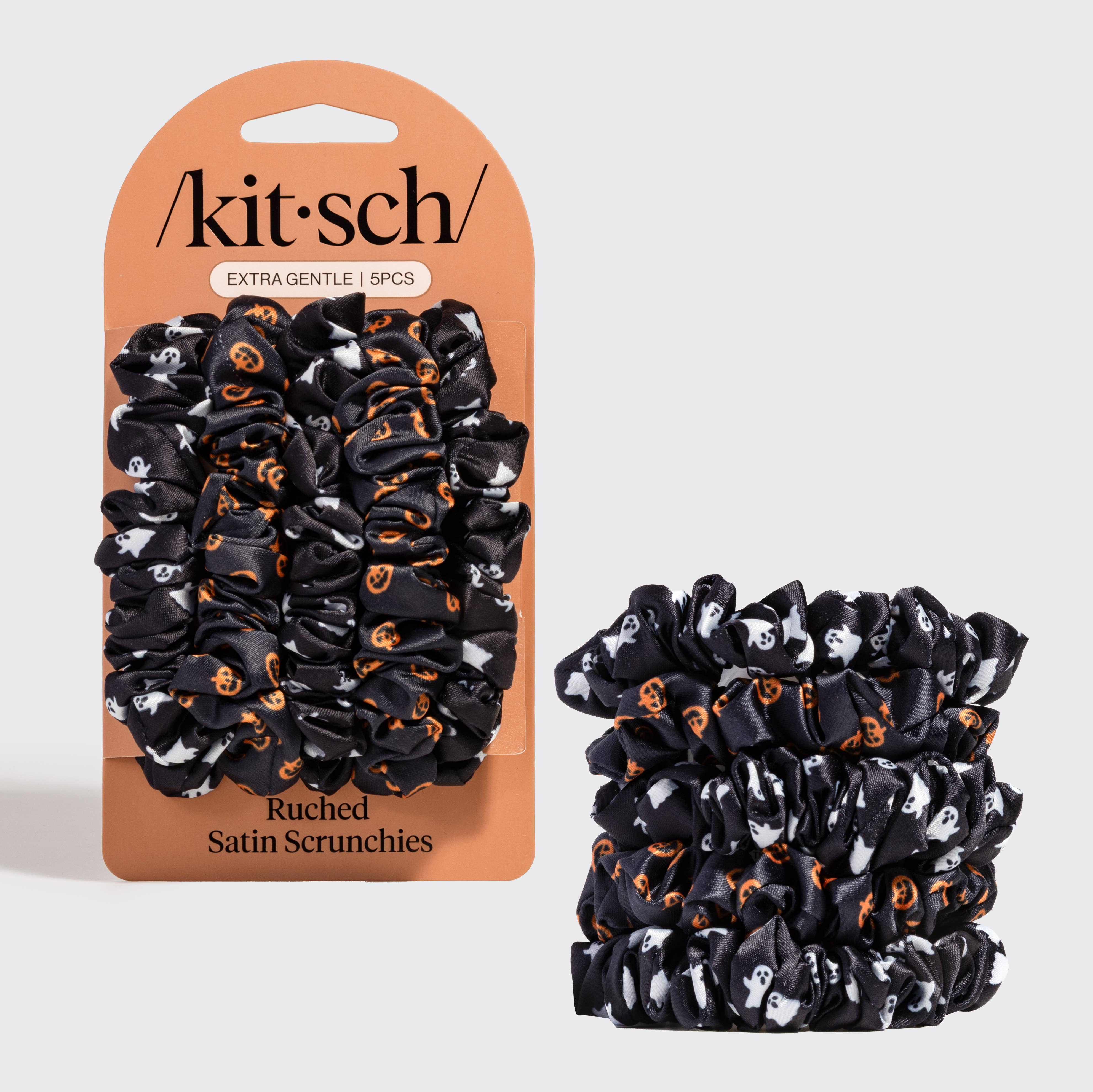 A 5-pack of Kitsch satin scrunchies in a black, white, and orange Halloween pattern, shown both in their retail packaging and as a loose stack on a light gray background.