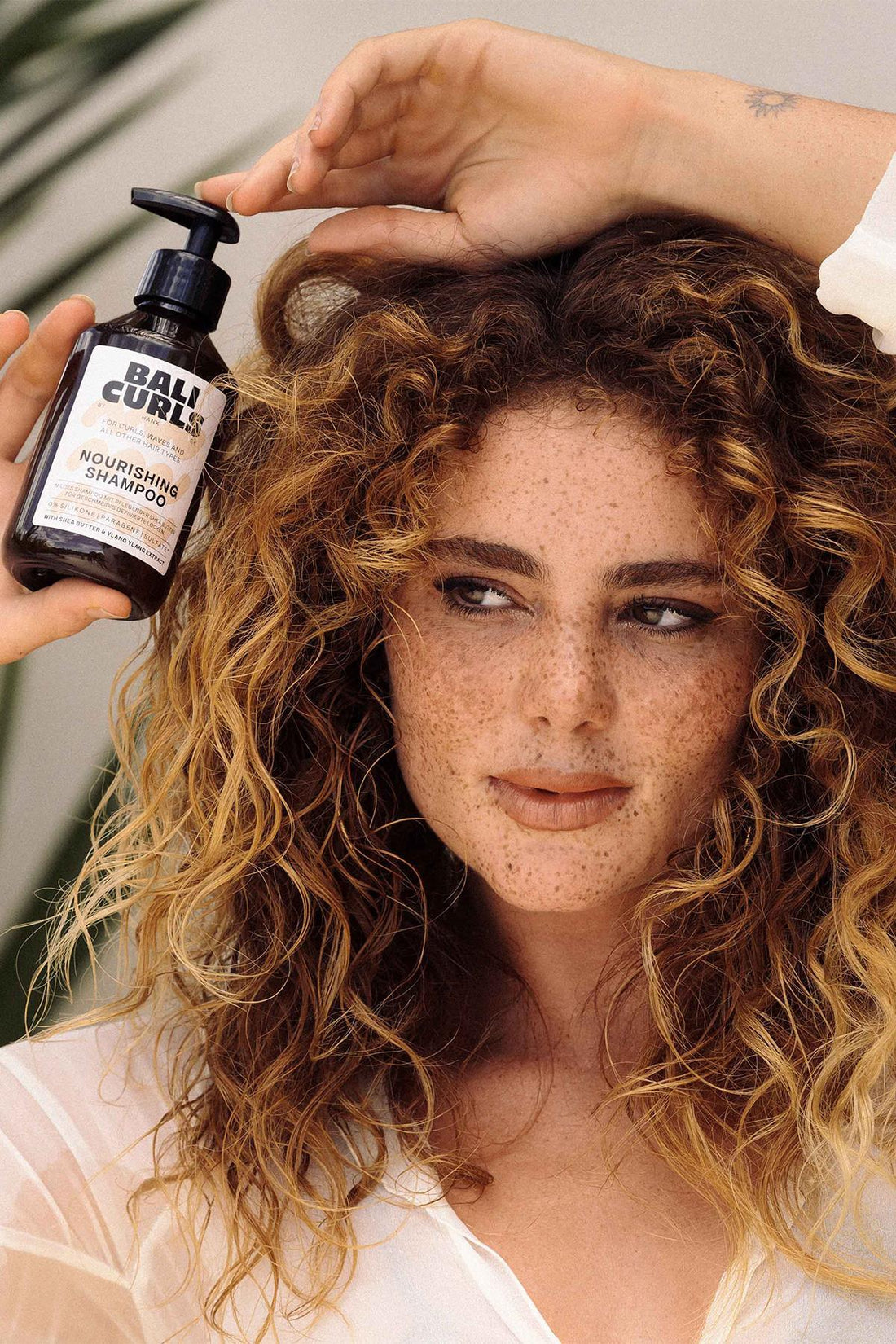 Woman with curly hair holding a bottle of Bali Curls shampoo.