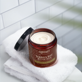 Jar of Qhemet Burdock Root Butter Cream on a white towel with a tiled wall background