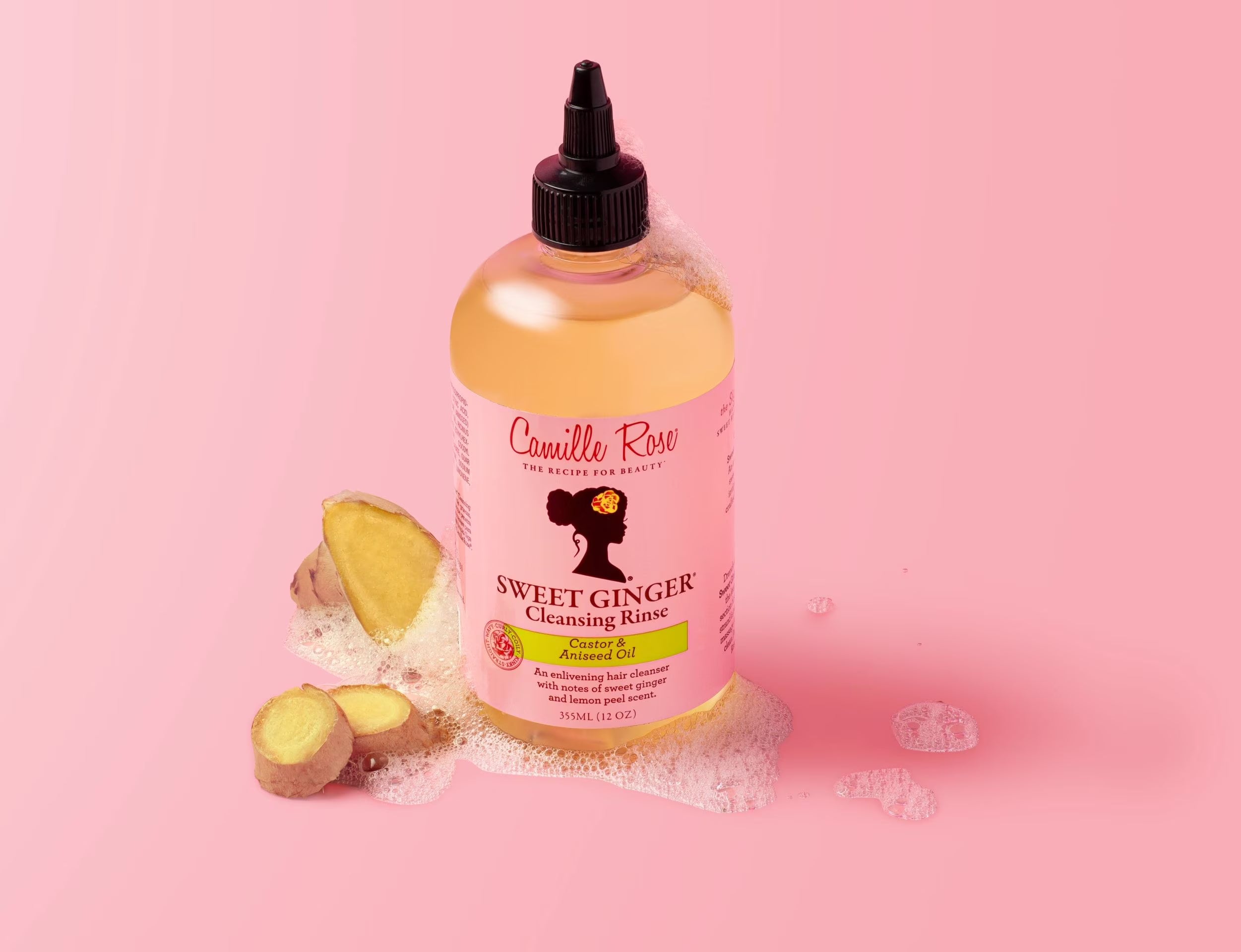 Bottle of Camille Rose Sweet Ginger Cleansing Rinse on a pink background with ginger roots.