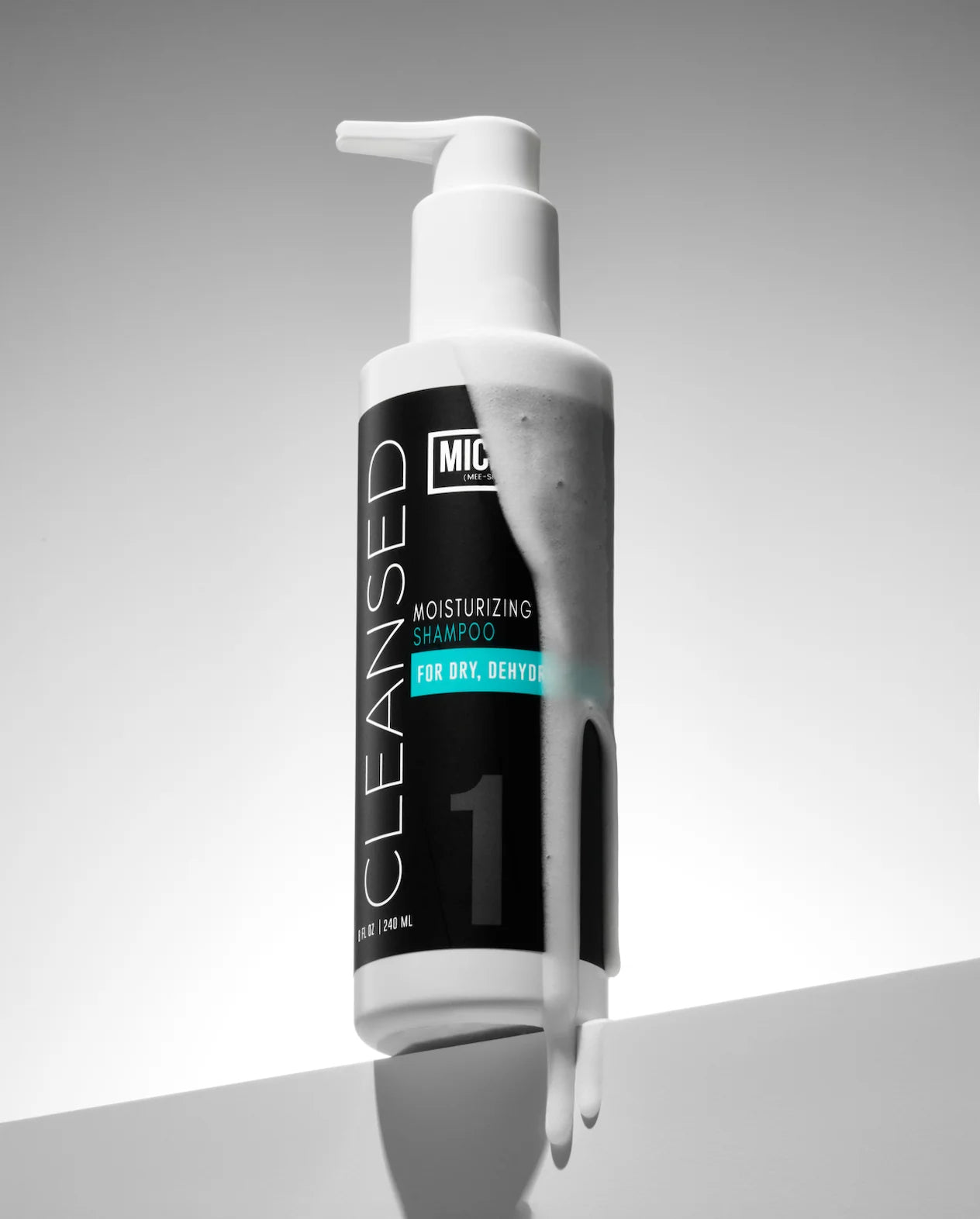 A bottle of Miche Moisturizing Shampoo for dry, deryver hair, shown with white shampoo dripping from the top of a matte black bottle against a gray gradient background.