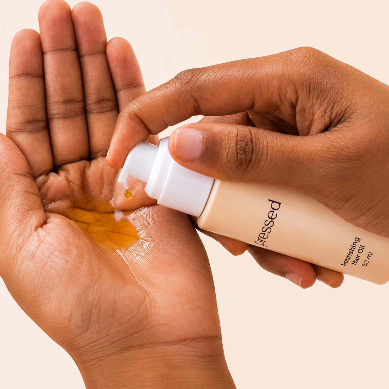 close-up of hands dispensing pressed nourishing hair oil 50ml from a pump bottle into the palm on a light background