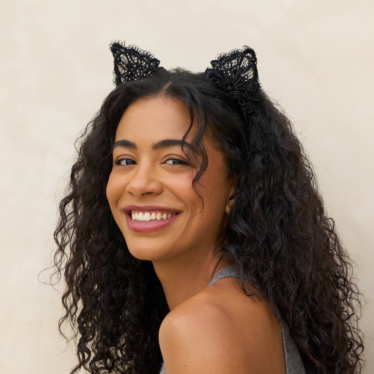 Woman wearing black cat ears against a beige background