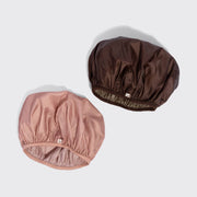 Two satin-like hair caps shown on a light gray background, one in dusty pink and one in dark brown. Each cap has an elastic gathered edge and a small white brand tag near the lower edge.