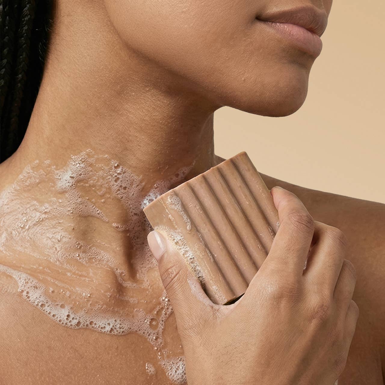 Person using a Vegan body wash bar with rich foamy lather on shoulder against a beige background