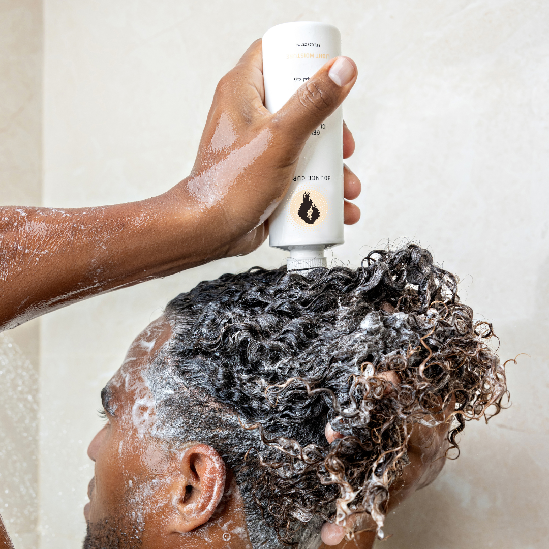Person applying shampoo to their hair with a bottle labeled Bounce Curl Gentle Clarifying Shampoo