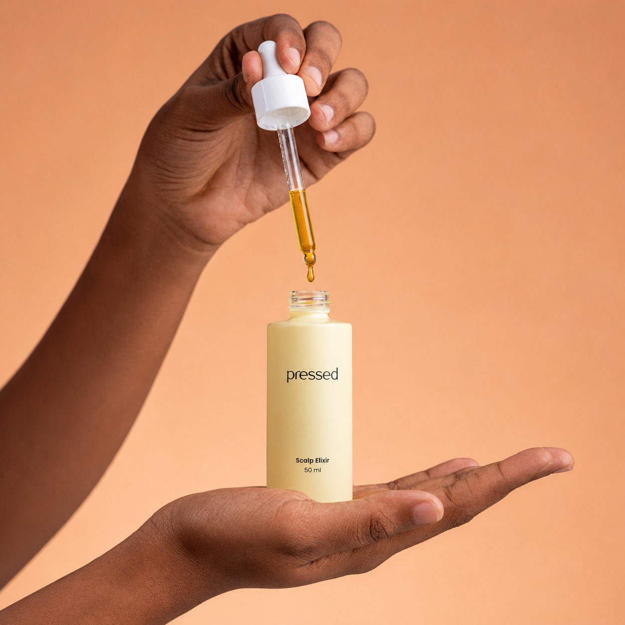 hand holding a pressed scalp elixir 50ml bottle while a dropper dispenses golden scalp oil above it against a warm beige background