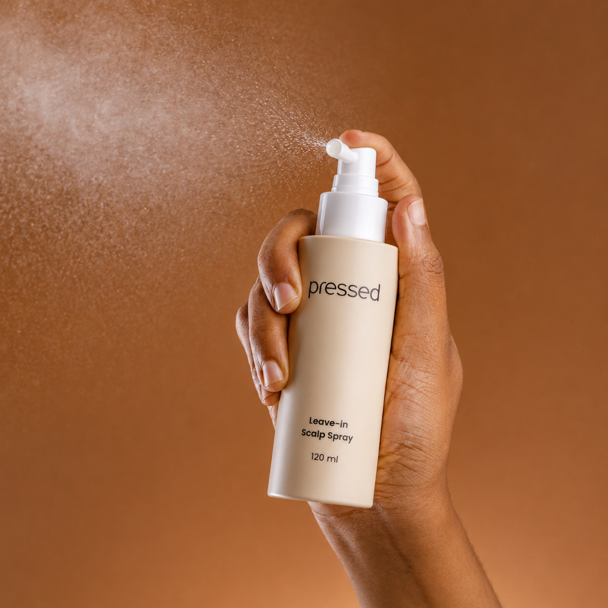 hand spraying pressed leave-in scalp spray 120ml with a fine mist against a warm brown background
