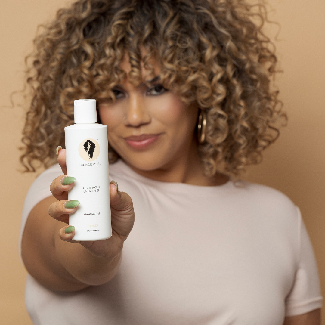 Woman holding a bottle of 'Bounce Curl' product against a beige background
