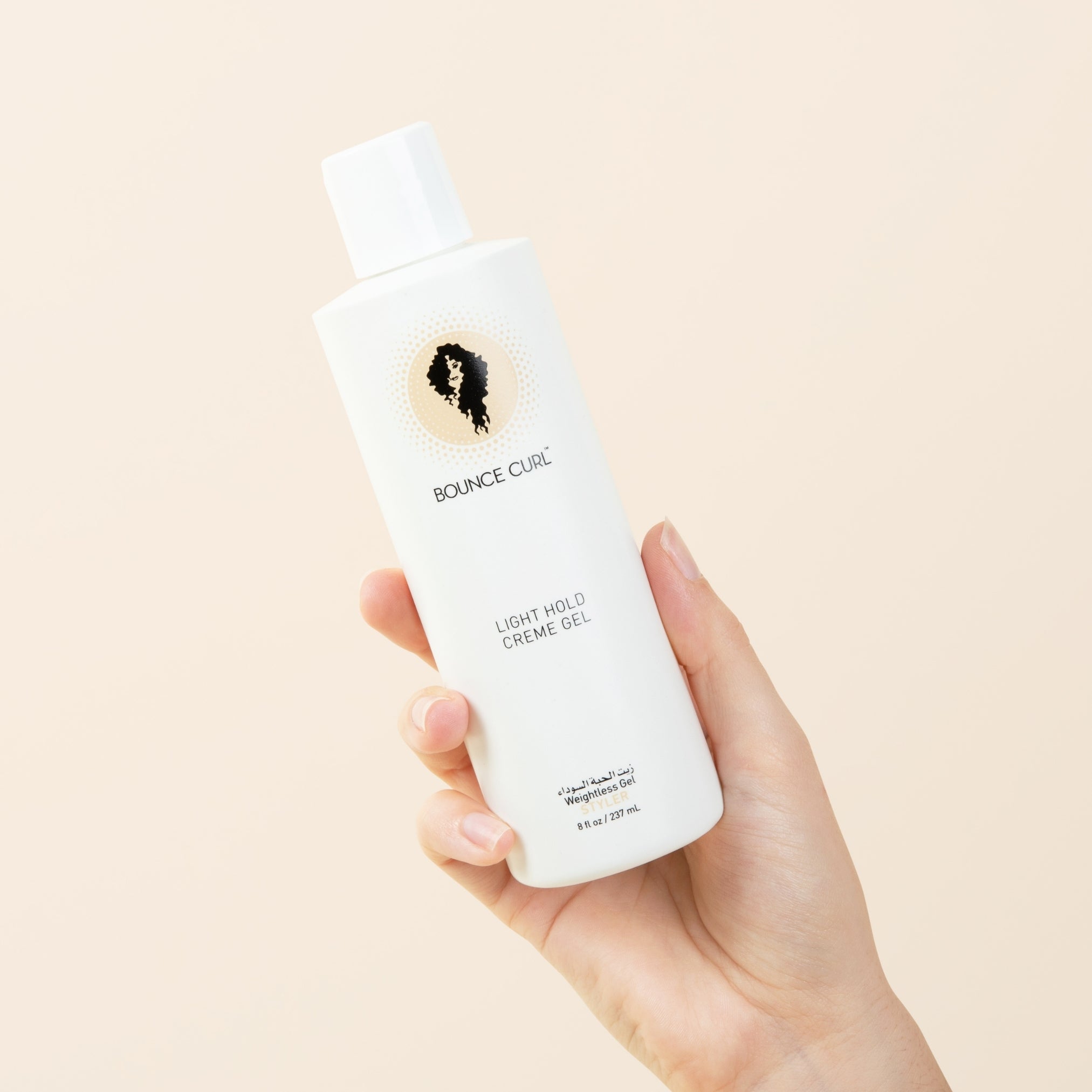A hand holding a white bottle of Bounce Curl Light Mold Creme Gel against a solid pale beige background.
