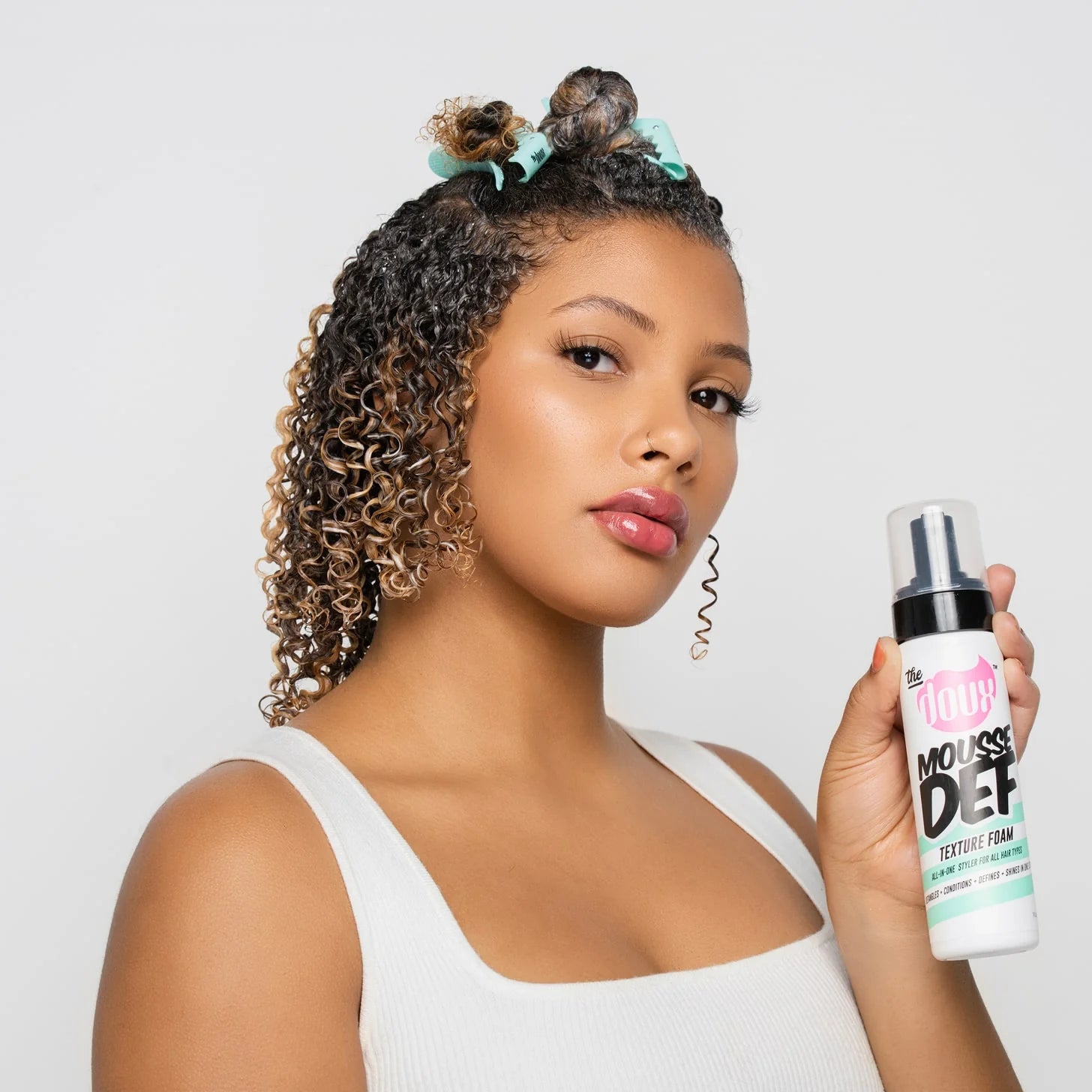 Woman holding a bottle of the doux Mousse Def product with a plain background
