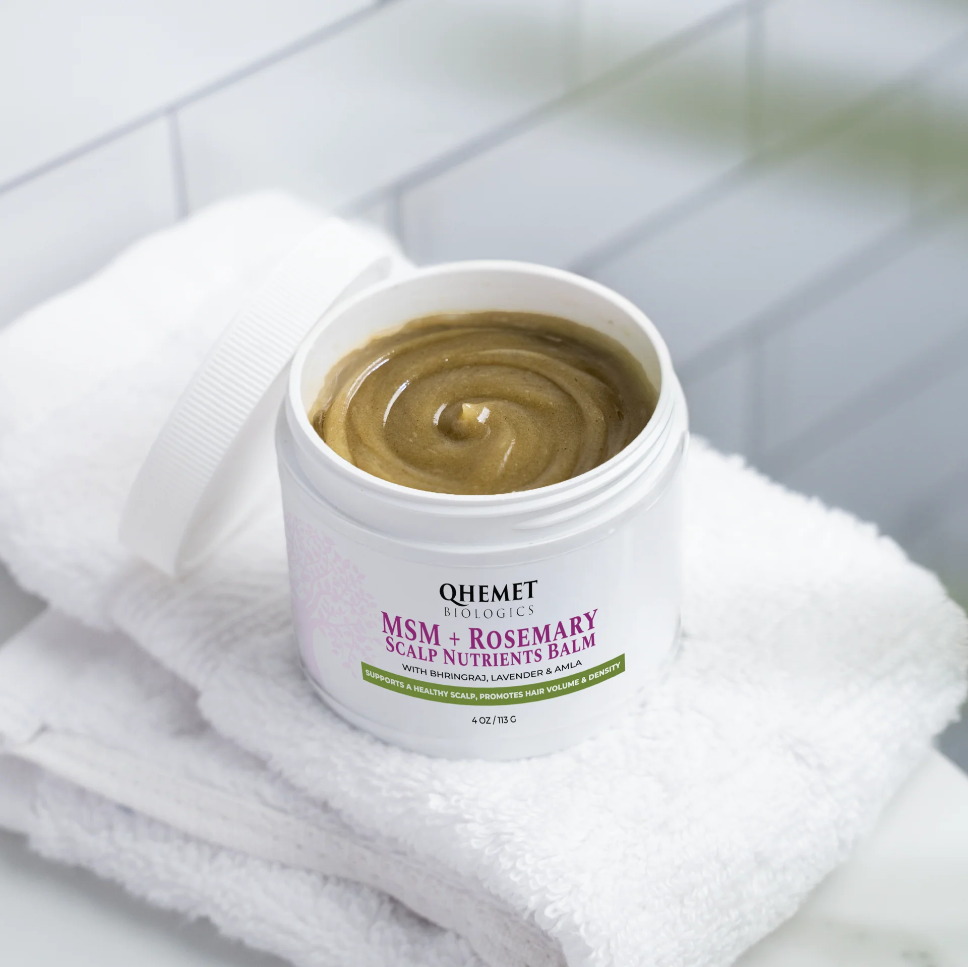 Balm container labeled 'QHemet' on a towel with a blurred background