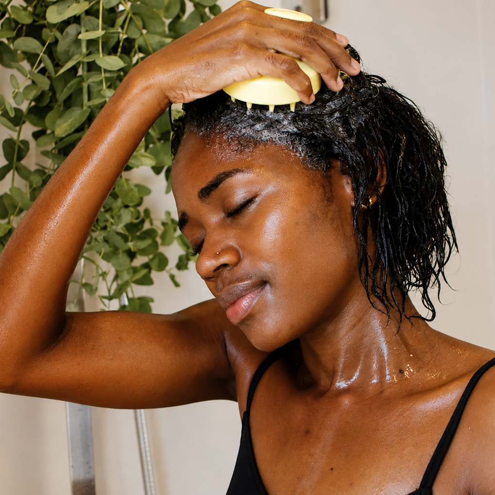 person using the pressed shampoo brush to massage shampoo into the scalp in the shower, demonstrating a relaxing scalp cleansing routine.