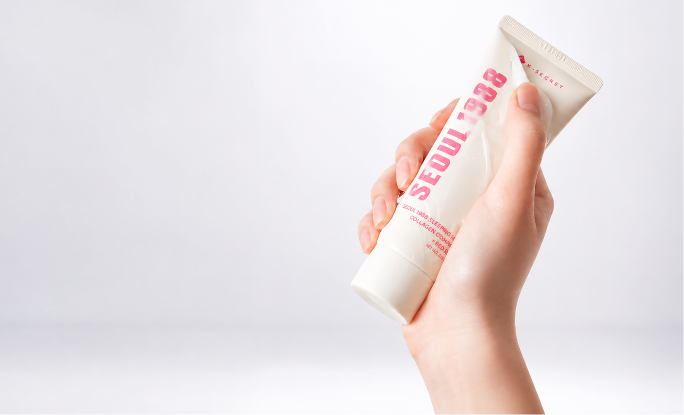 Hand holding a tube of k-secret seoul 1988 sleep mask product with visible branding on a white background