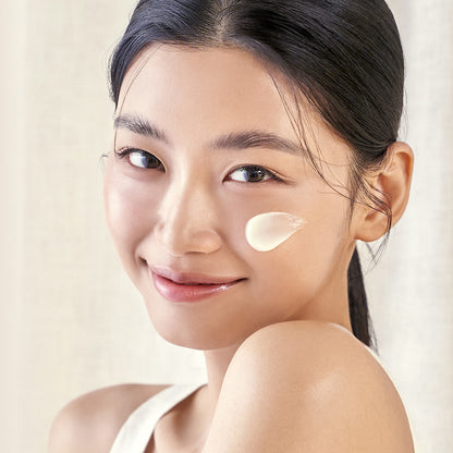 Woman with a skincare product applied to her cheek against a neutral background